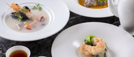 Una mesa de comedor con platos de mariscos, una tetera y dos recipientes pequeños con salsa.