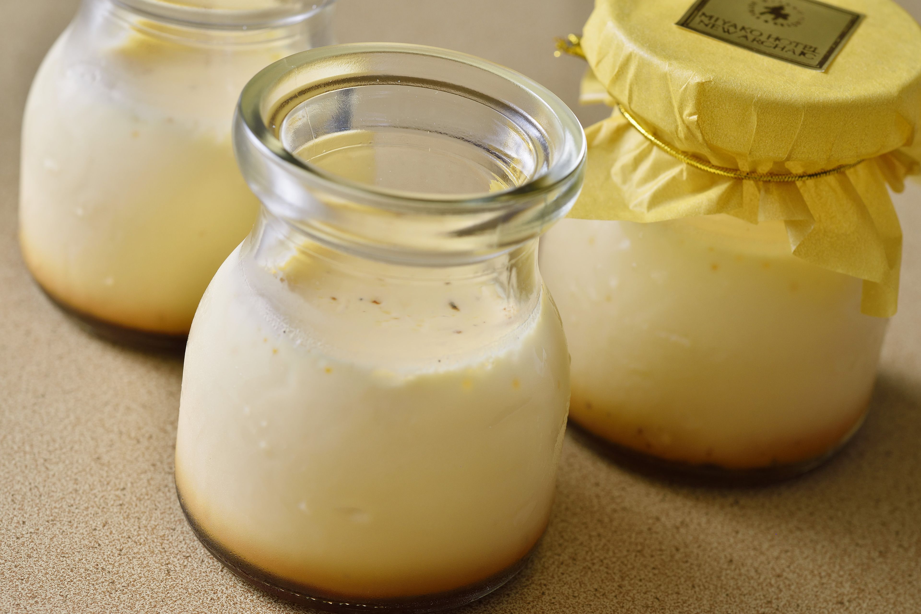 Three glass jars with a yellow label, containing a white substance, possibly a dairy product.