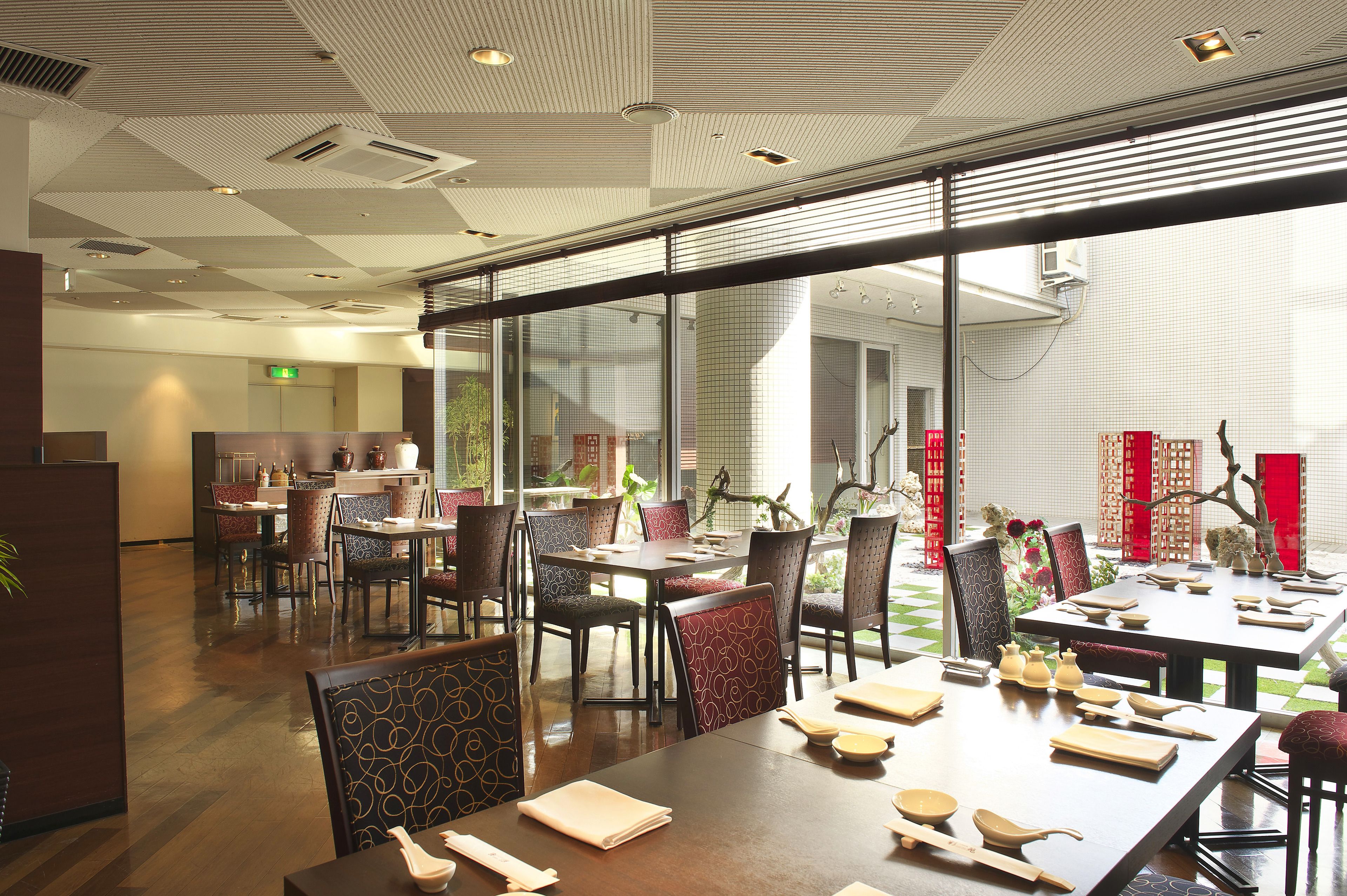 Un restaurante con varias mesas y sillas, ventanas amplias y un diseño de techo moderno.