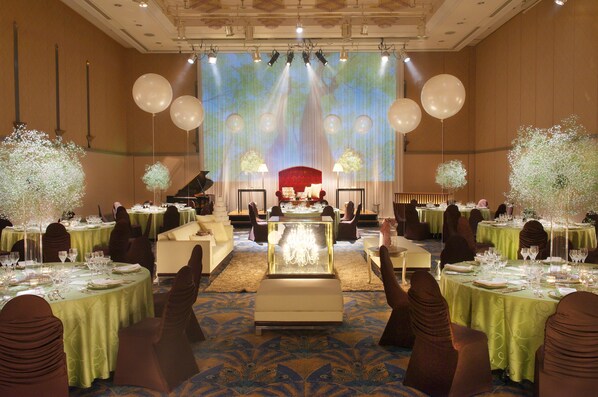 A banquet hall with round tables, chairs, and a stage with a piano.