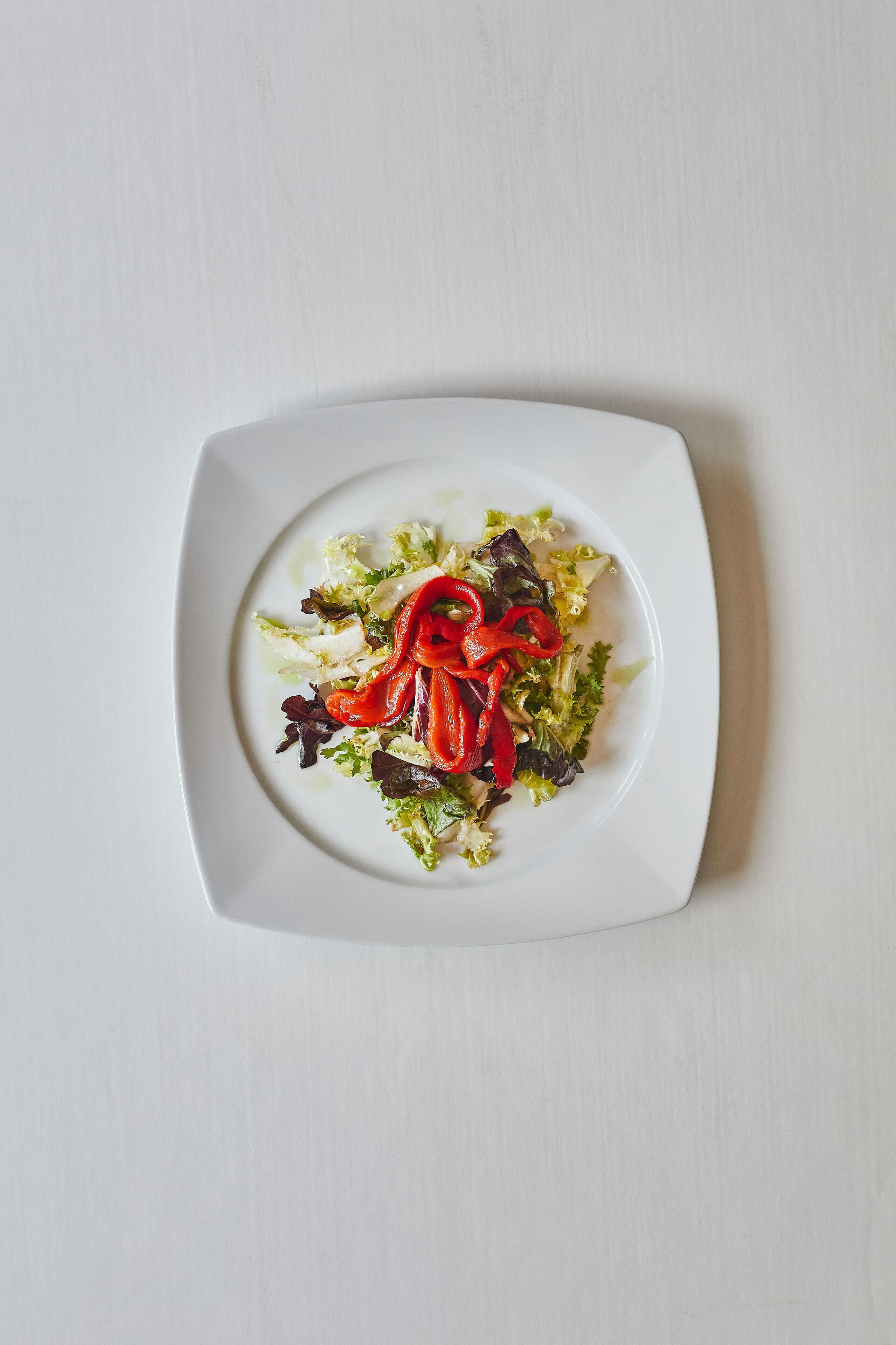 A white plate with a salad on a white table.