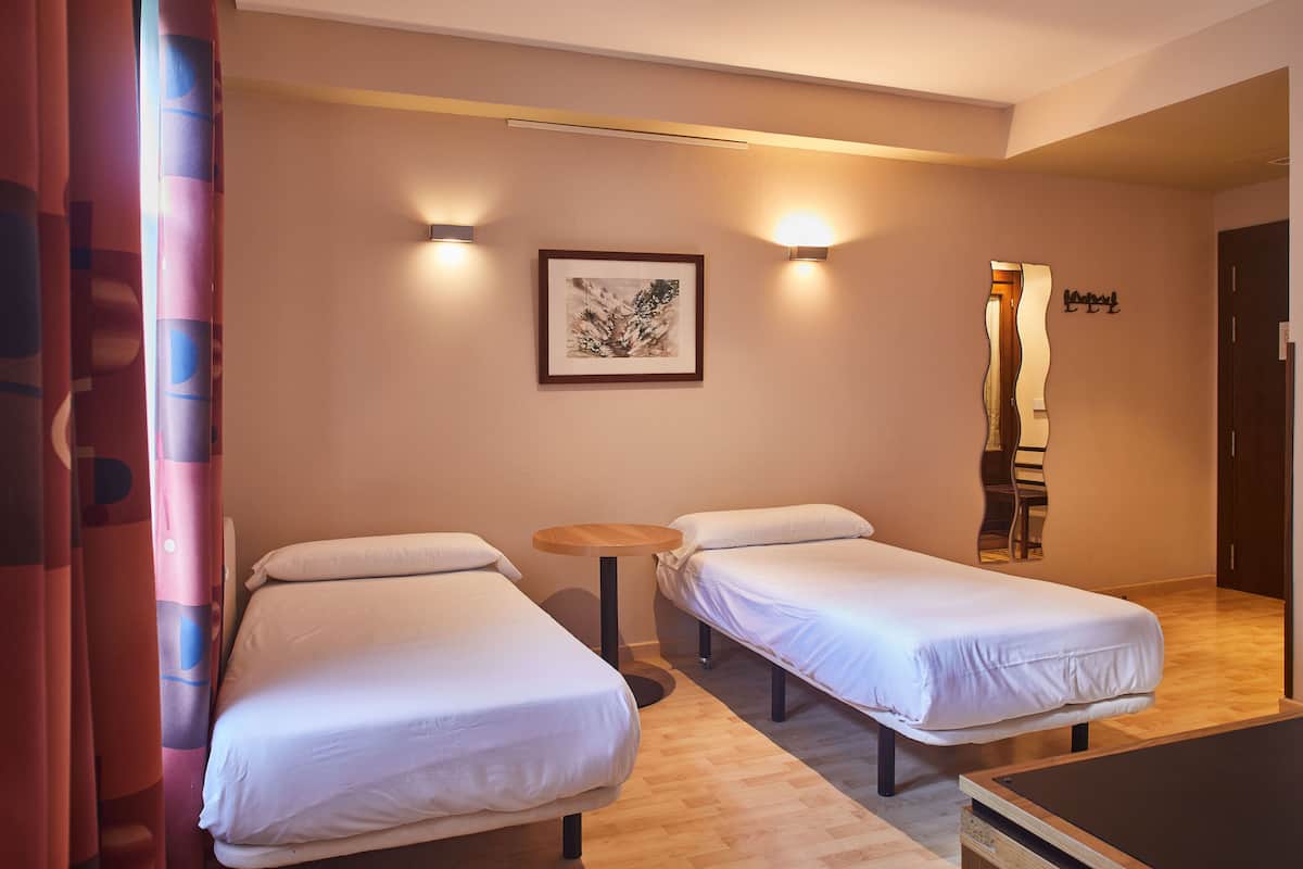 A hotel room with two single beds, a small round table, and a framed artwork on the wall.