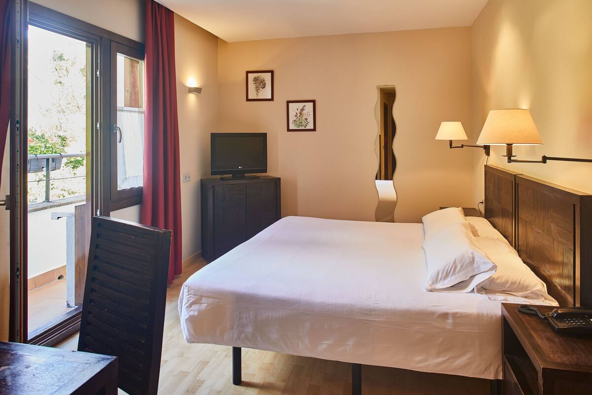 A hotel room with a bed, a desk, a television, and a window with curtains.
