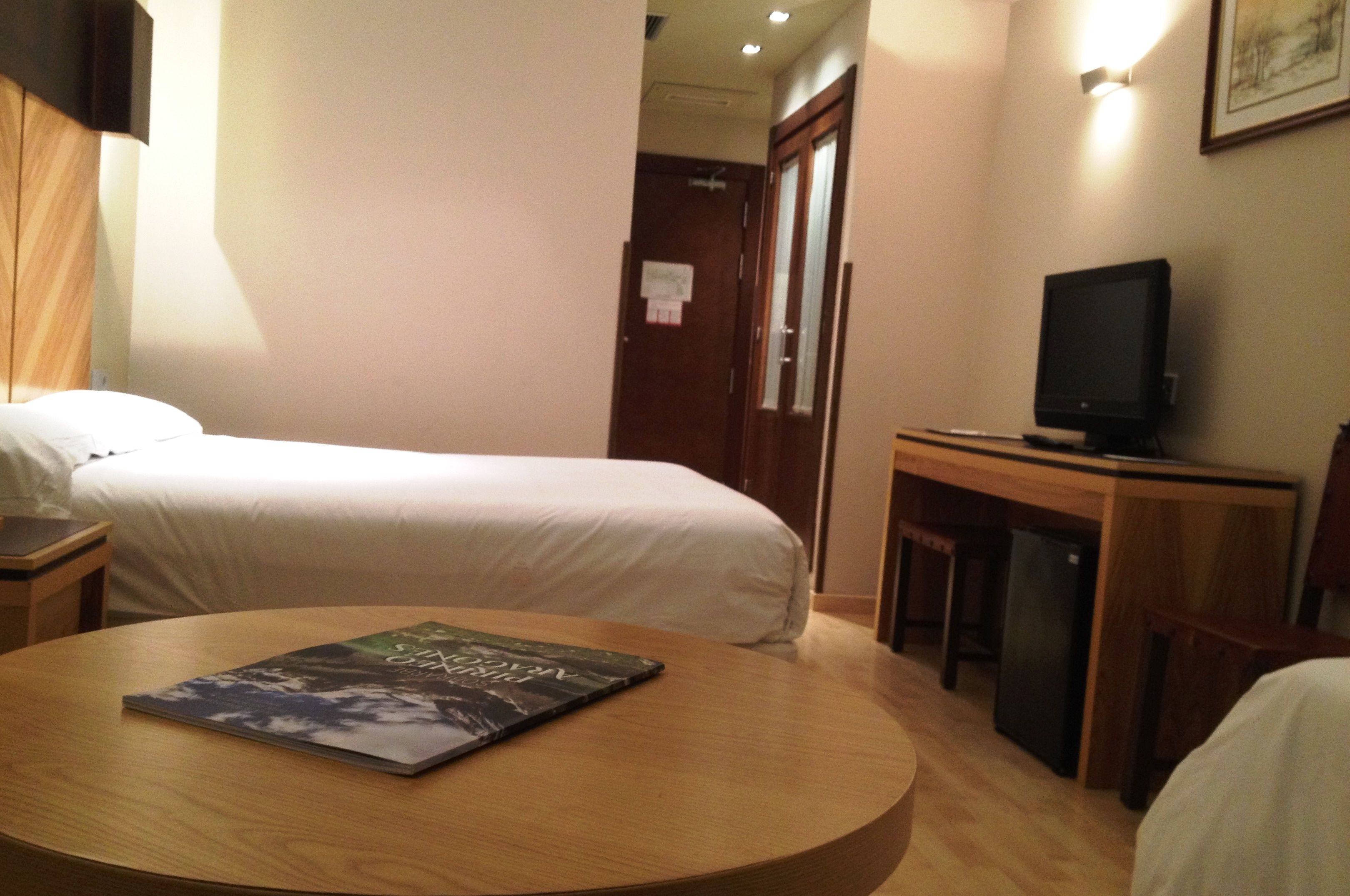 Habitació d'hotel amb un llit, una taula de treball amb televisió i una taula rodona amb un llibre.