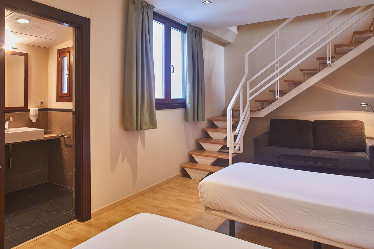 A bedroom with a bed, a sofa, a staircase, and a bathroom with a sink.
