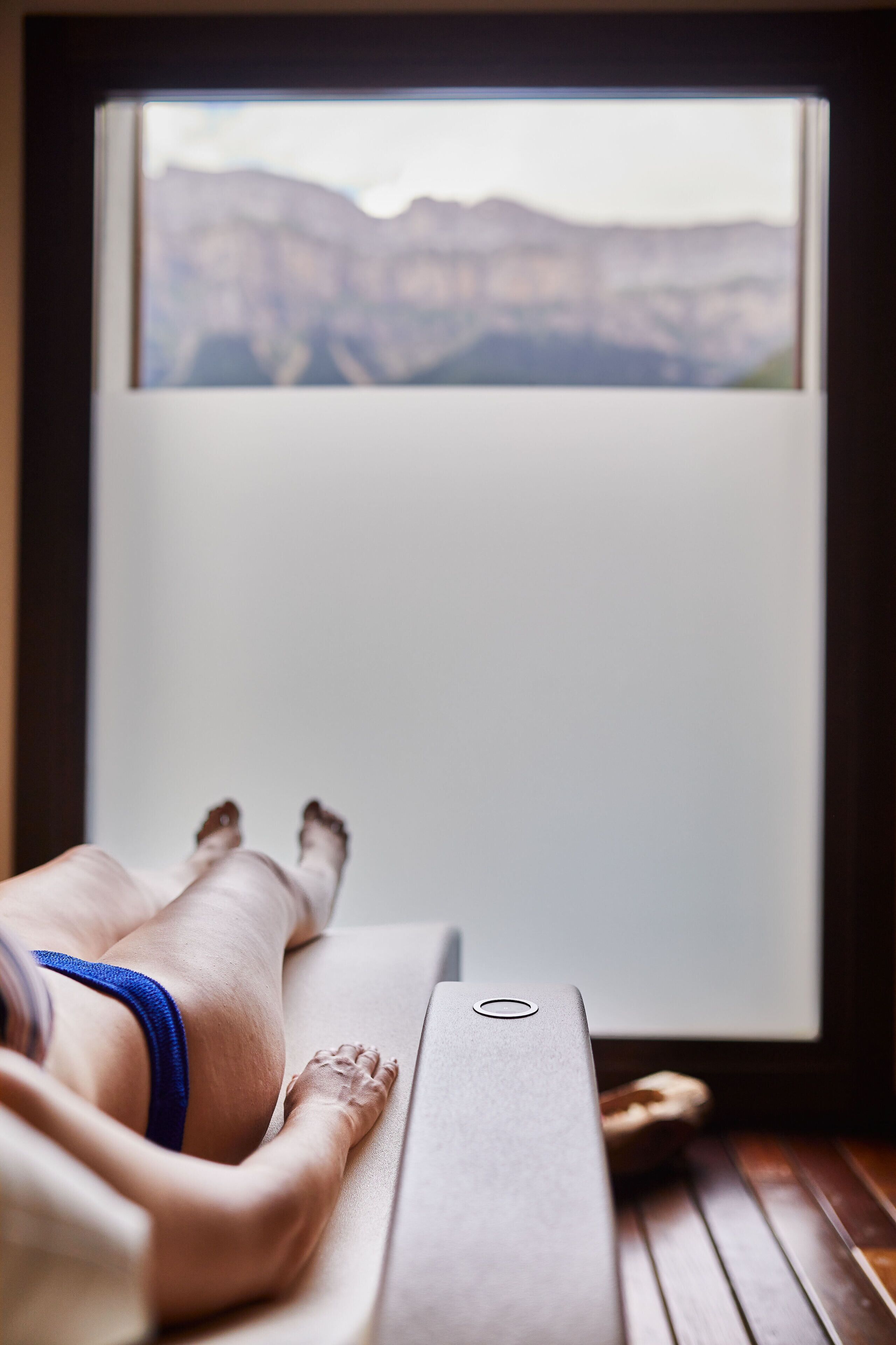 A person lying on a massage table with a window view of mountains.