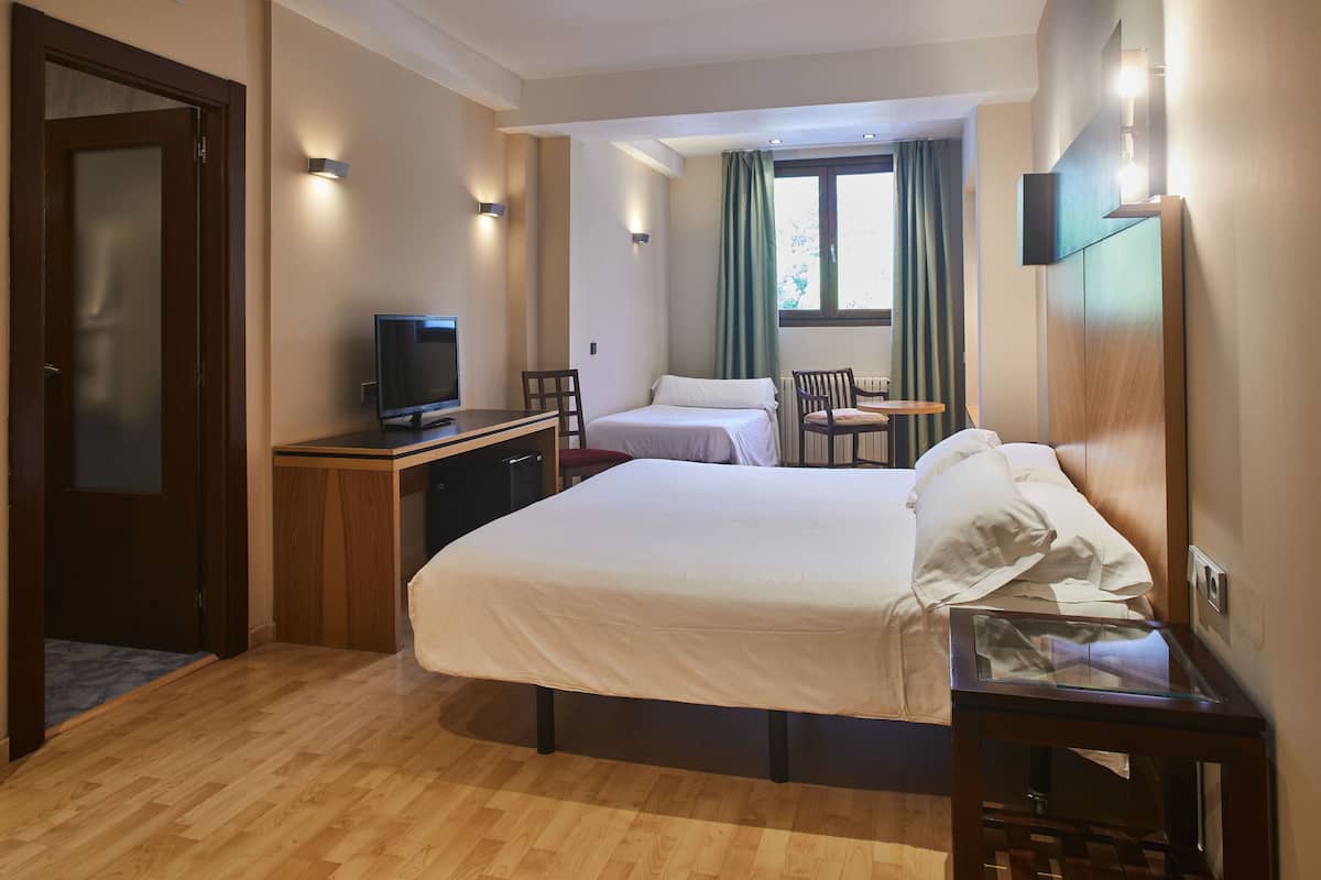 A hotel room with a large bed, a desk with a television, a chair, and a small table.