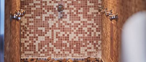 A tiled shower with a mosaic pattern, a metal faucet, and a pebble-lined floor.