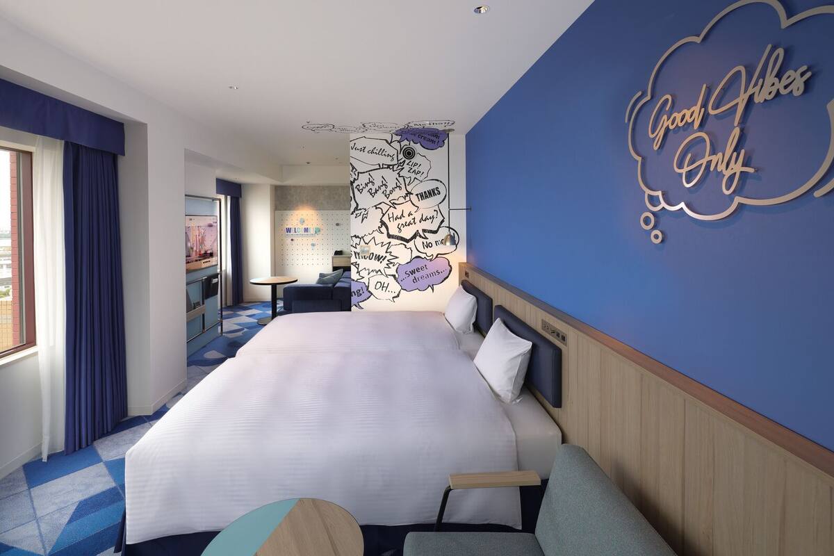 Habitación de hotel con una cama grande, una mesita pequeña, una pared con un letrero que dice 'Good Vibes Only' y un mural en la pared.