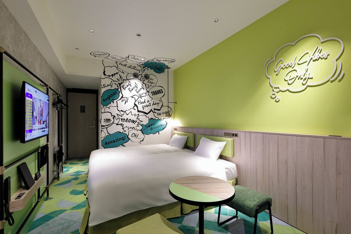 Una habitación de hotel con una cama, una mesita, un televisor y un letrero en la pared que dice 'Good Vibes Only'.