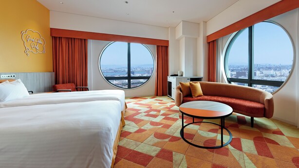 A hotel room with two beds, a sofa, a small table, and large windows offering a city view. - Hotel Kintetsu Universal City (Osaka)