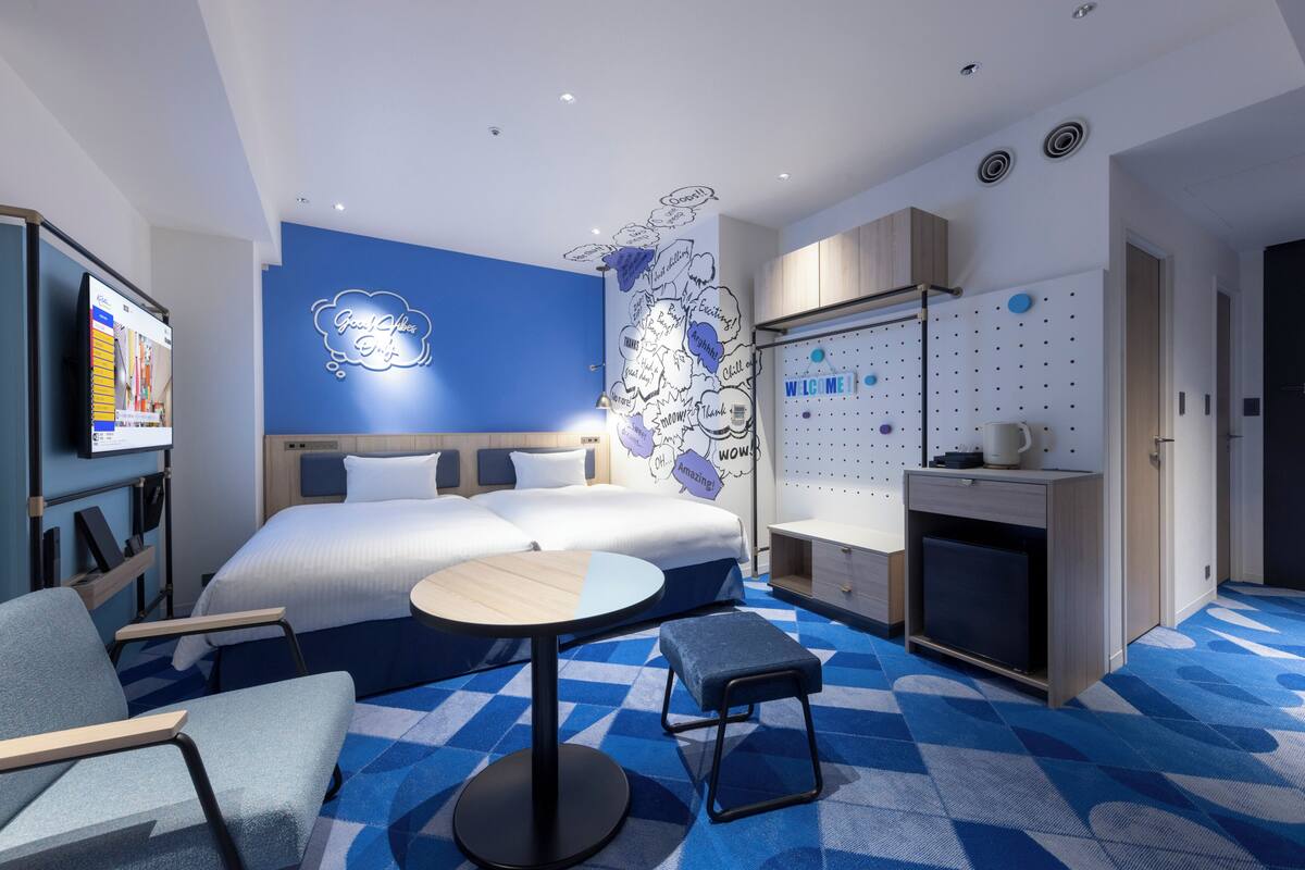Habitación de hotel moderna con una cama grande, un escritorio, una silla, una mesita, un televisor y una pared con un mapa del mundo y bocadillos de conversación.