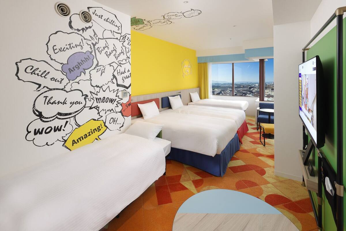 Habitación de hotel con tres camas, vista a la ciudad, un ventanal grande y una pared con bocadillos de diálogo.