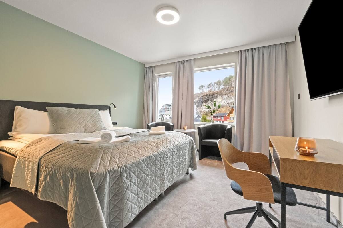 A hotel room with a bed, a desk, a chair, and a TV.