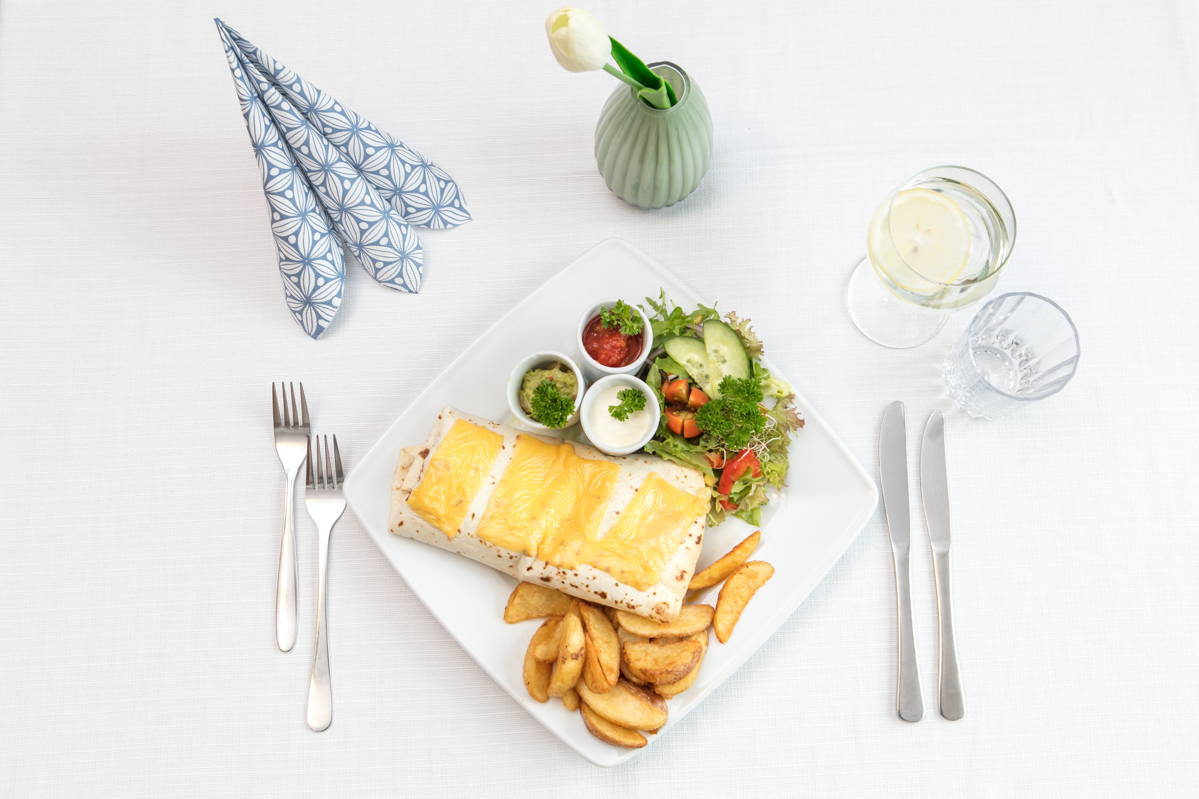 A meal with a fish fillet, fries, salad, and drinks on a white table.