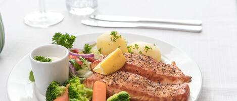 Un plato con salmón, brócoli, zanahorias y patatas, acompañado de un recipiente pequeño con salsa.