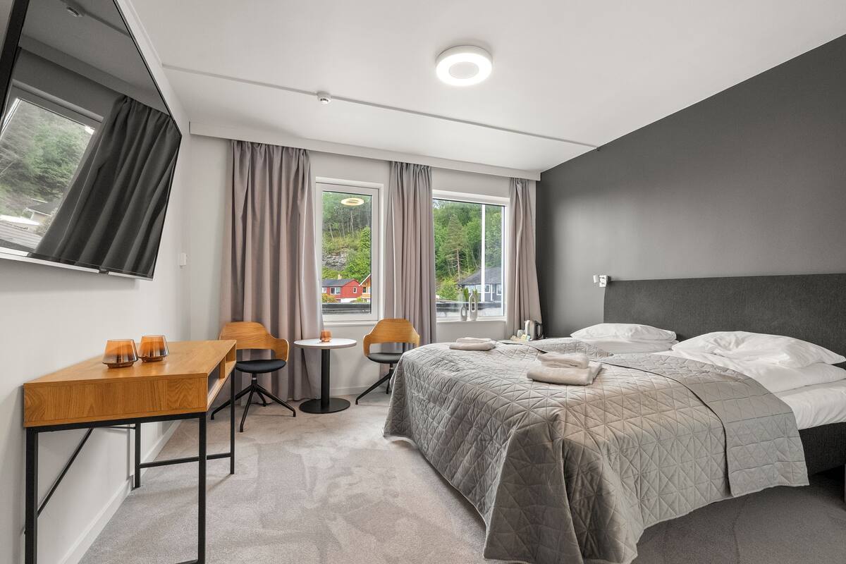 A modern hotel room with a bed, a desk, a chair, and a small table.