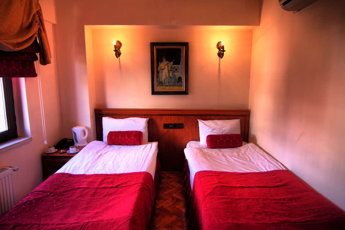 A hotel room with two beds, a painting on the wall, and a window with curtains.