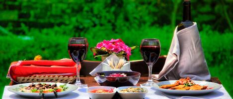 Mesa posta com refeição, copos de vinho e garrafa de vinho, com um fundo verde ao ar livre.