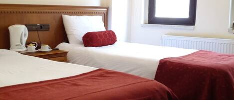 A hotel room with two beds, a painting on the wall, a window with curtains, and a radiator.