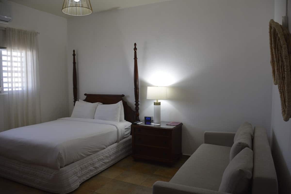 Quarto com cama de dossel, mesa de cabeceira com abajur e um sofá.