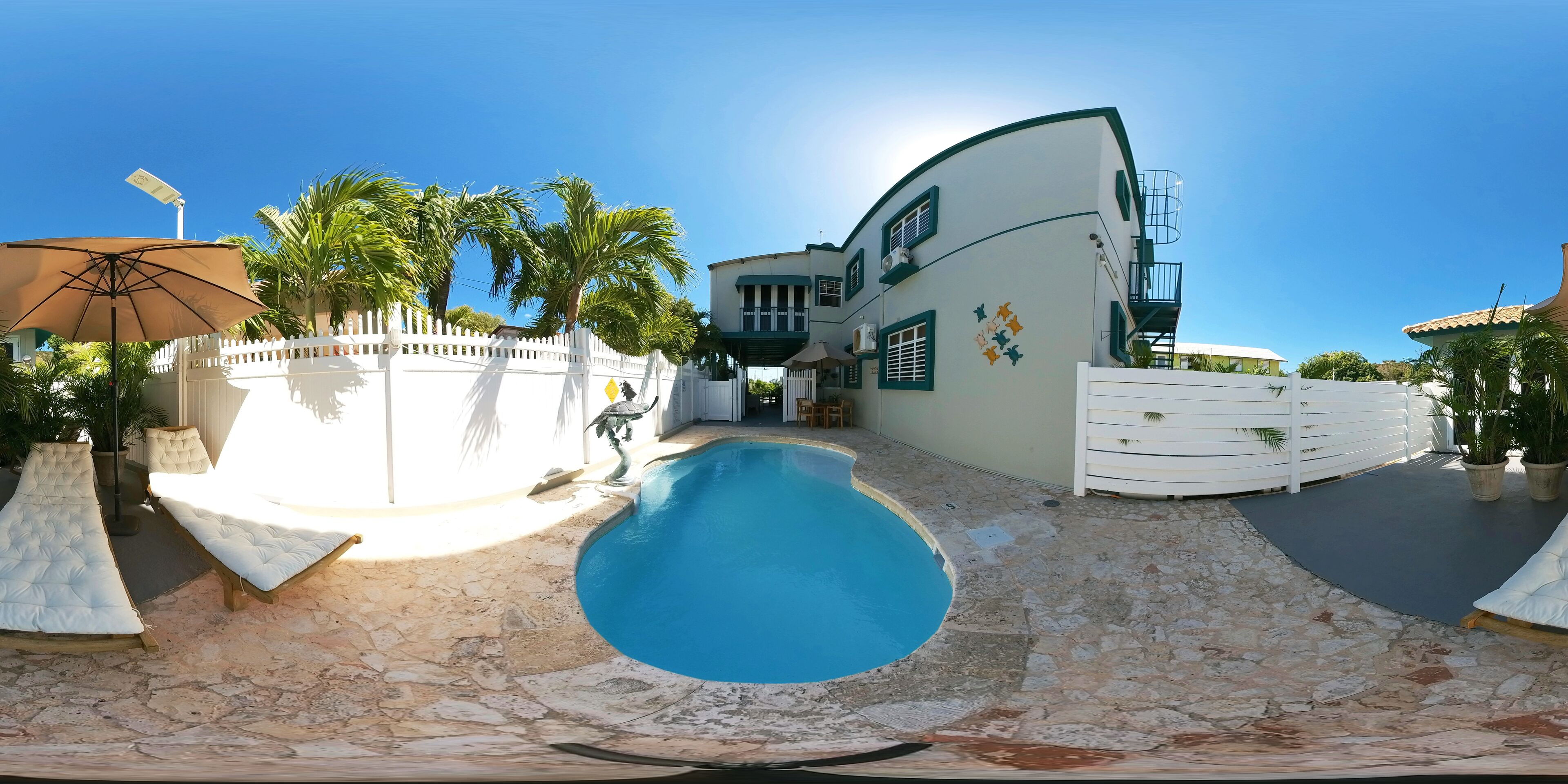Uma piscina com espreguiçadeiras, um cercado branco e um edifício com telhado curvo.