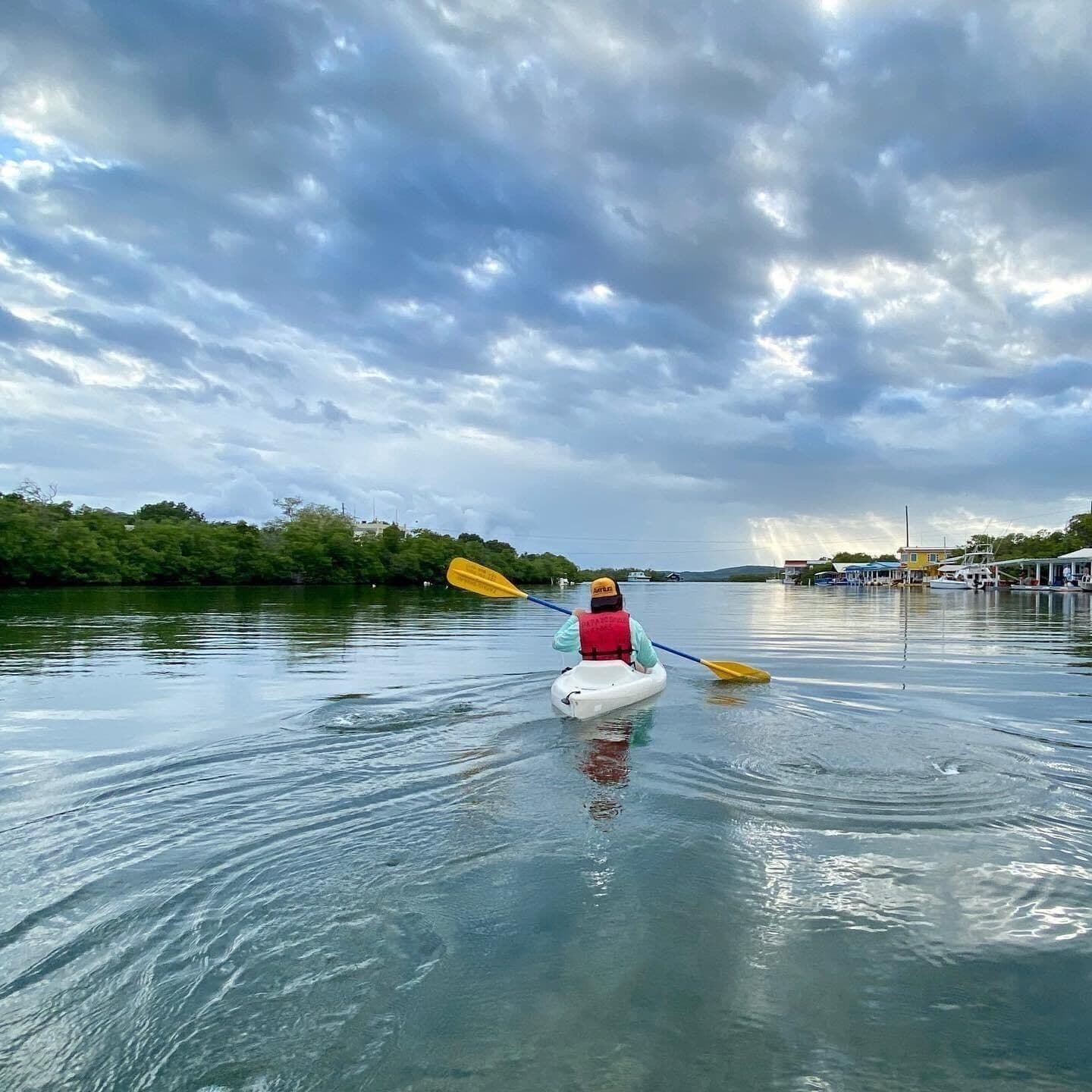 Una persona fa kayak su un fiume calmo sotto un cielo nuvoloso.