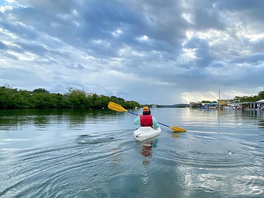 Una persona fa kayak su un fiume calmo sotto un cielo nuvoloso.