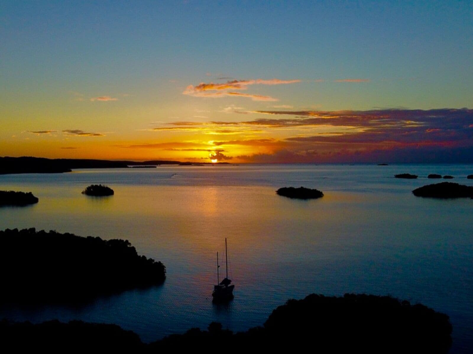 Un tramonto sull'acqua calma con una barca ancorata al centro.