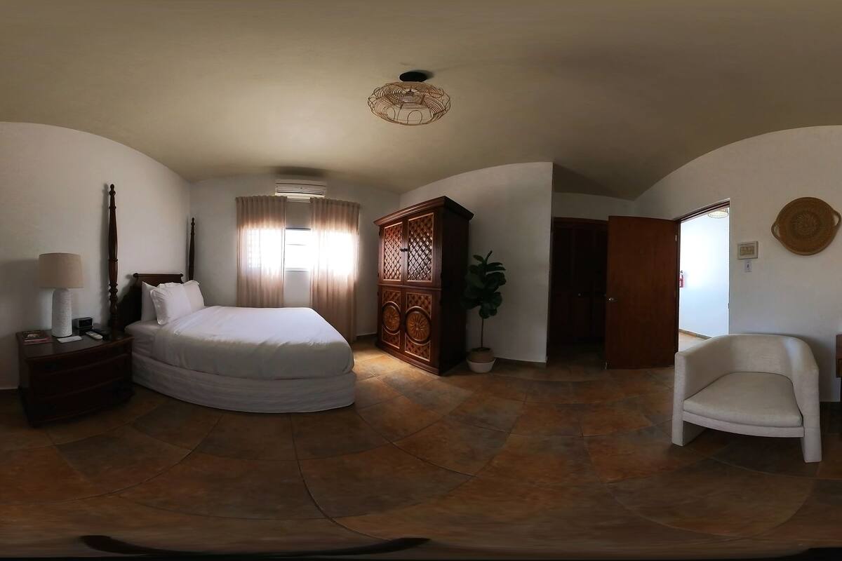 Quarto com cama, mesa de cabeceira, luminária, cadeira, armário e planta em vaso.