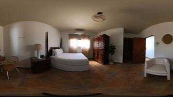 A bedroom with a bed, a nightstand, a lamp, a chair, a cabinet, and a potted plant.
