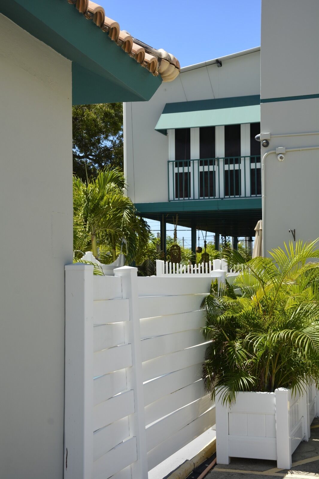 A white building with a balcony, a white picket fence, and lush greenery.