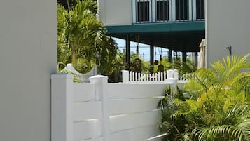 A white building with a balcony, a white picket fence, and lush greenery.