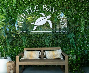 A wooden bench with two pillows in front of a wall with a turtle logo and the words "Turtle Bay Inn" and "Hotel La Parquera".