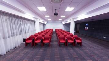 A conference room with rows of red chairs, a projector, and a carpeted floor.