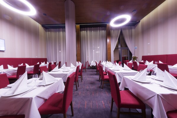 Un restaurante con mesas dispuestas para comer, sillas tapizadas en rojo y suelo alfombrado.