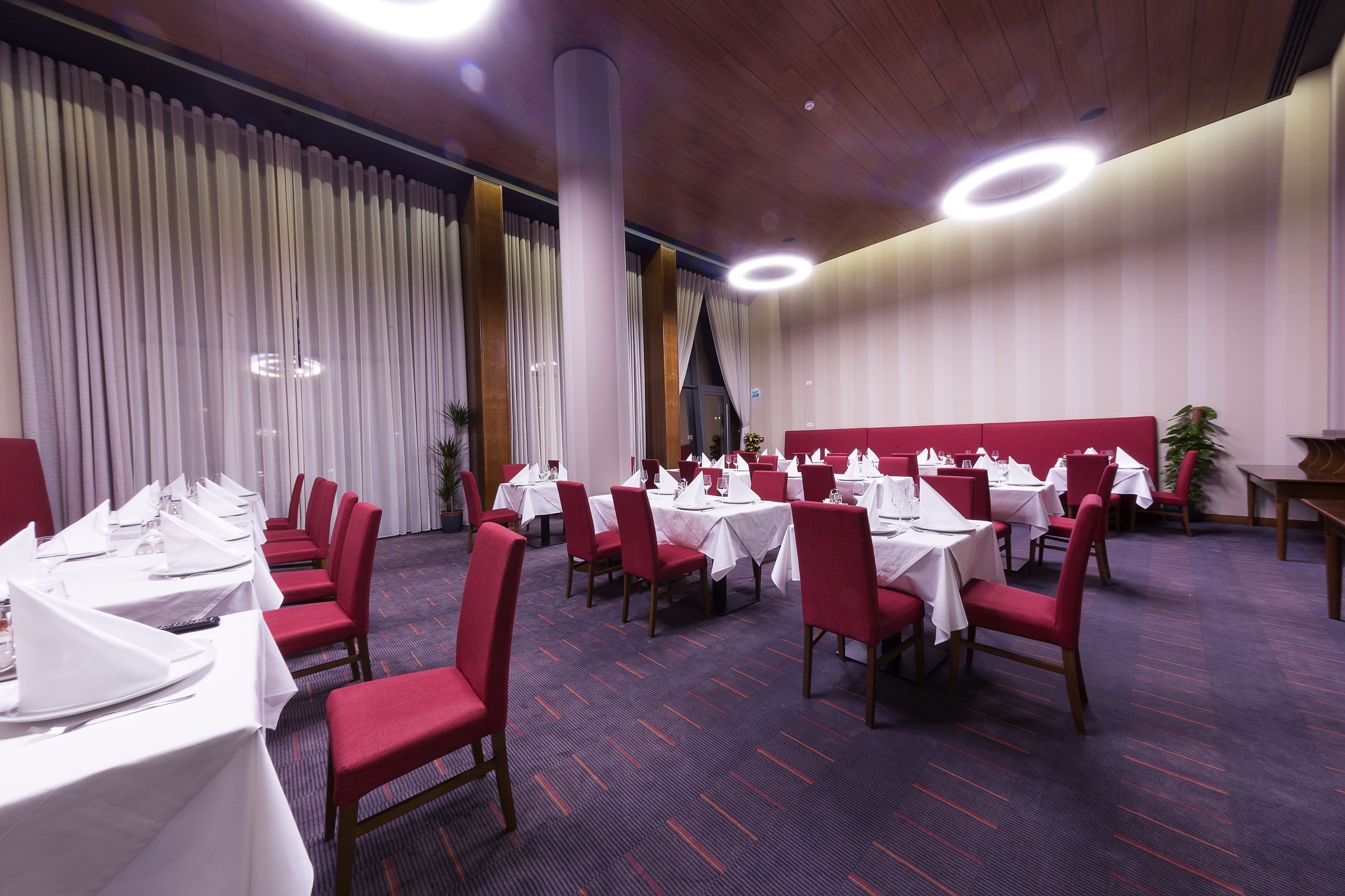 Un salón de banquetes con mesas redondas, sillas rojas y manteles blancos.