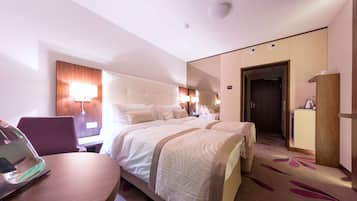 A hotel room with a large bed, a desk, a chair, a lamp, and a wardrobe.