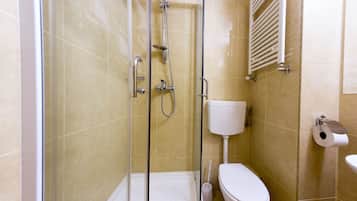 Un baño con ducha de vidrio, inodoro y dispensador de papel higiénico.