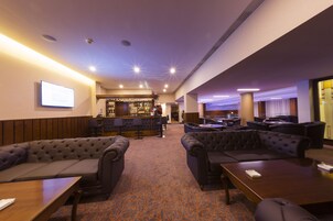 Un hall de hotel con una zona de bar, espacios de asiento y suelo alfombrado.