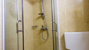 A glass-enclosed shower with a handheld showerhead, a handheld showerhead, and a handheld showerhead.