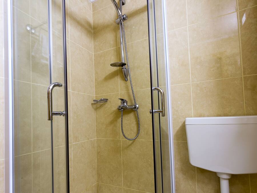 A glass-enclosed shower with a handheld showerhead, a handheld showerhead, and a handheld showerhead.