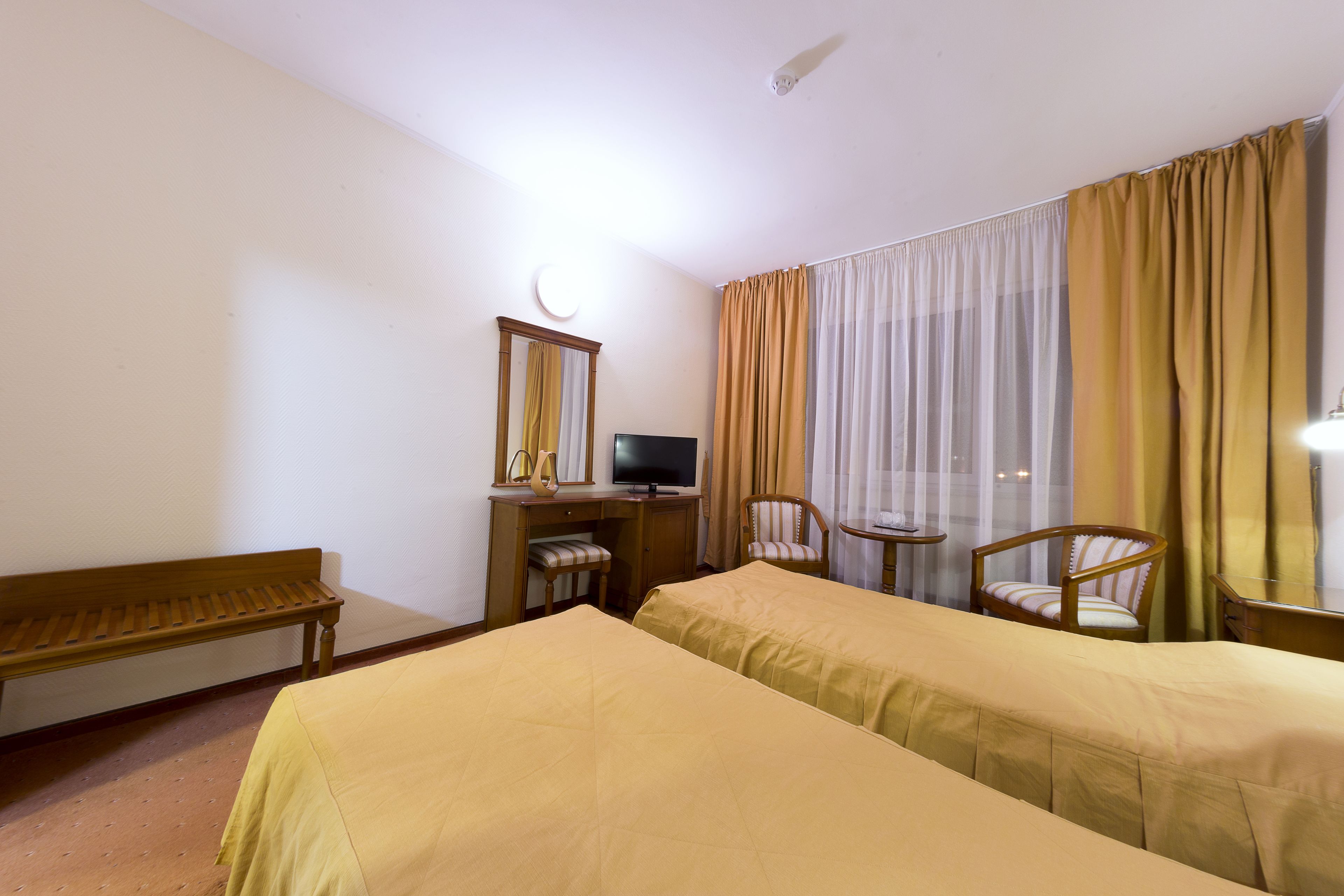 Habitación de hotel con dos camas, un escritorio con computadora, una silla y un banco.