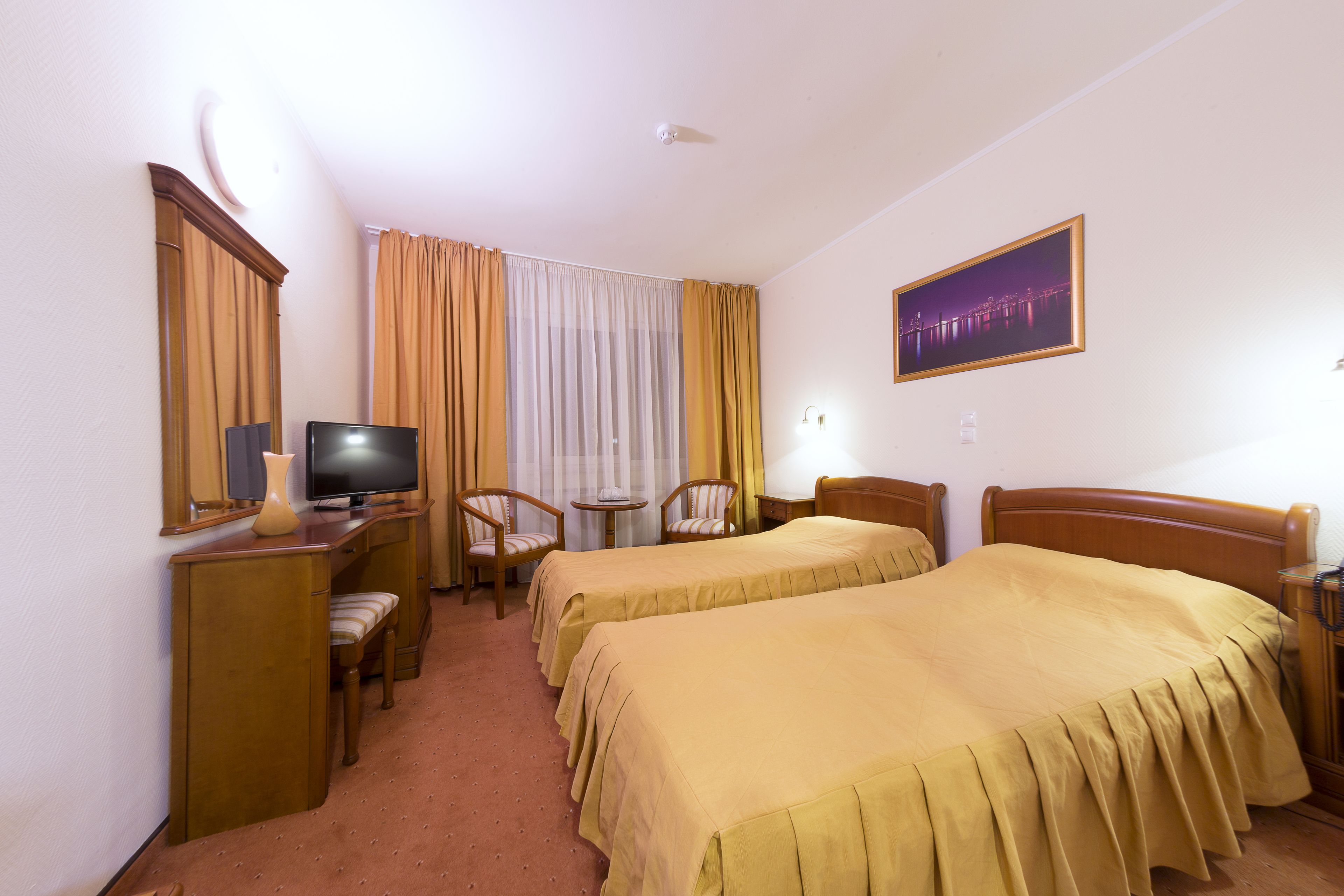 A hotel room with two beds, a desk with a television, a chair, and a small table.