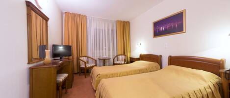 A hotel room with two beds, a desk with a television, a chair, and a small table.