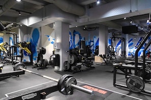 Une salle de sport équipée de matériel de musculation, de miroirs et ornée de peintures murales bleues.