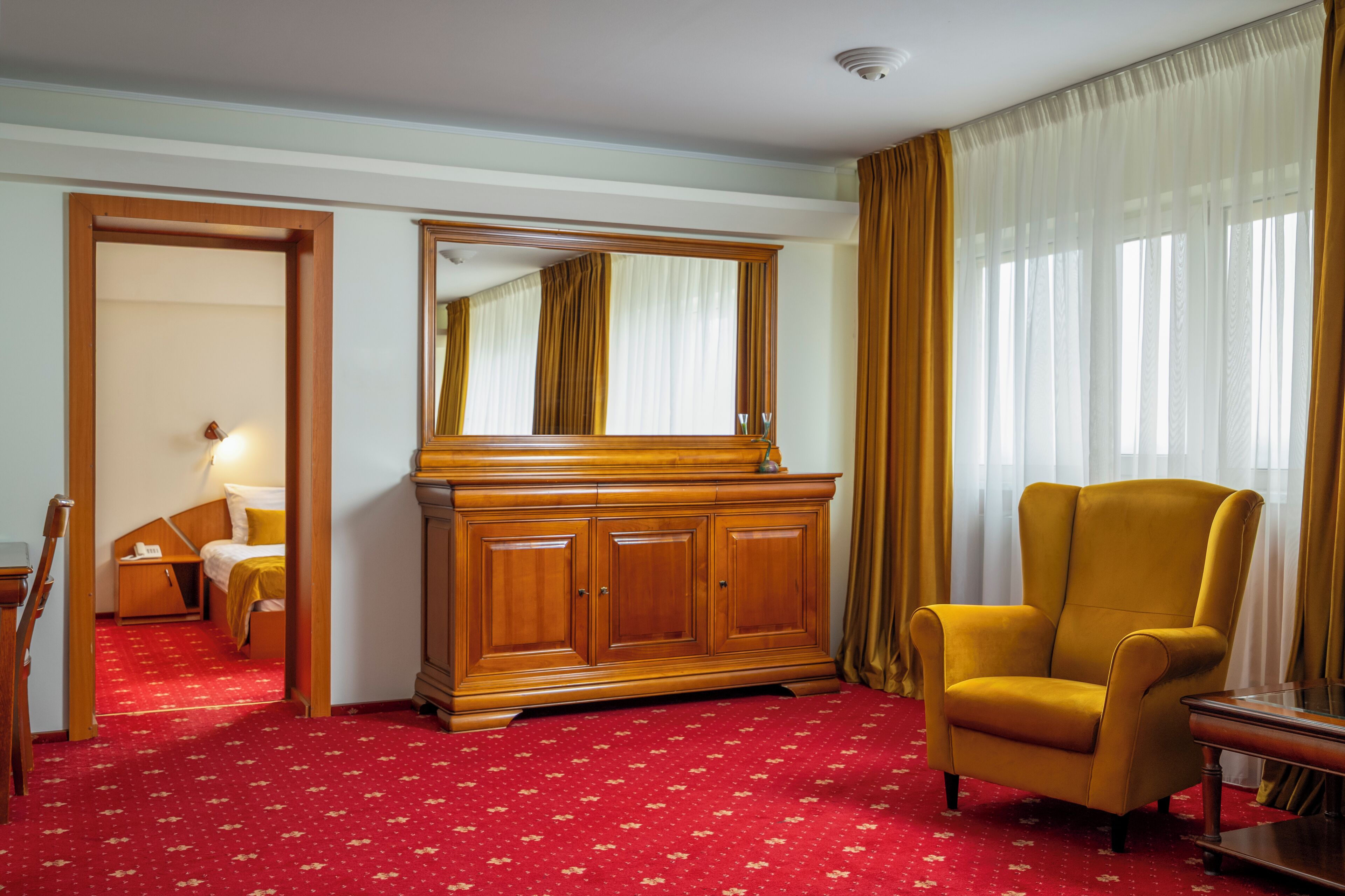 Ein Hotelzimmer mit einem Holzschrank, einem gelben Sessel, einem Bett und einem roten Teppich.