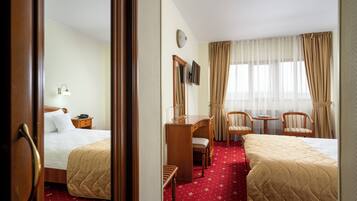 Ein Hotelzimmer mit zwei Betten, einem Schreibtisch, einem Stuhl, einem kleinen Tisch, einer Uhr und einem Fenster mit Vorhängen.