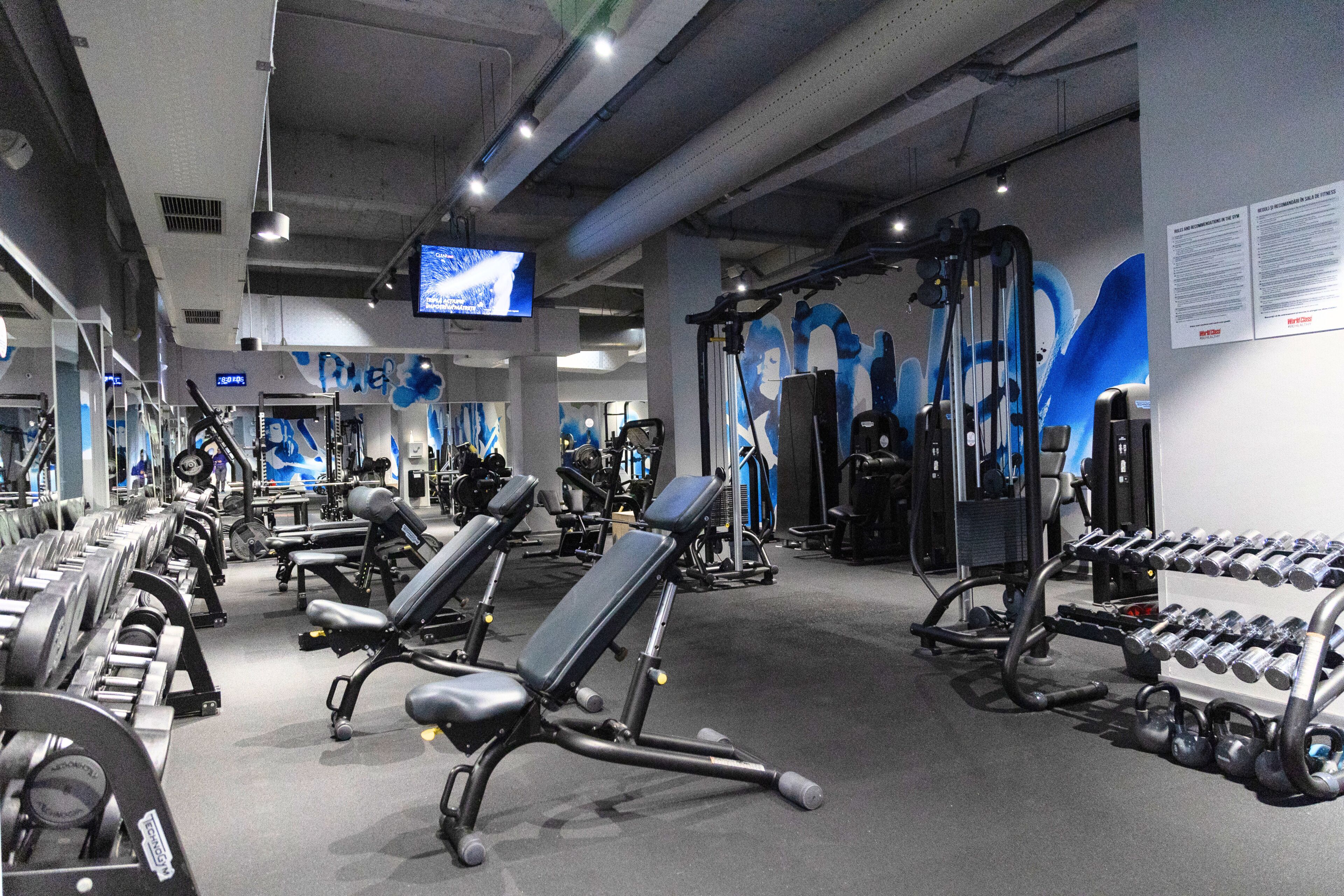 Un gimnasio con equipo de ejercicio, bancos y una pantalla de televisión.