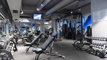 Un gimnasio con equipo de ejercicio, bancos y una pantalla de televisión.